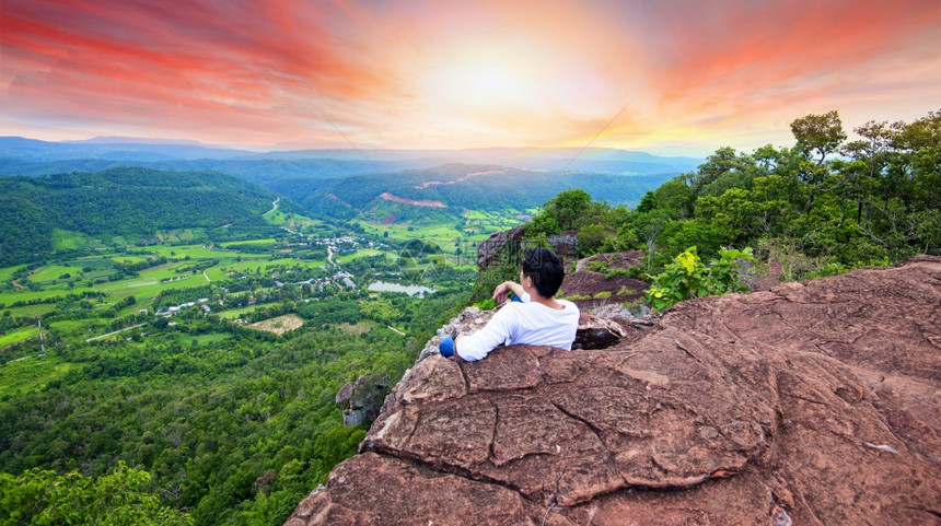 在山上的人坐在岩石谷悬崖上Man看着日落谷图片