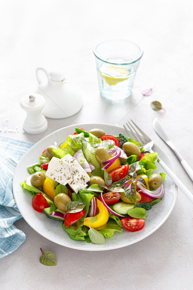 希腊沙拉新鲜蔬菜包括黄瓜西红柿橄榄洋葱胡椒白菜奶酪生和草药并配有盐胡椒和橄榄油图片