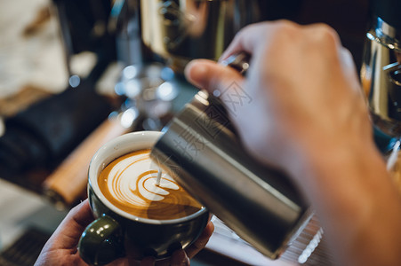 拿铁锹的人制作拿铁艺术的酒吧以牛奶和咖啡杯为焦点的镜头旧式过滤图像背景