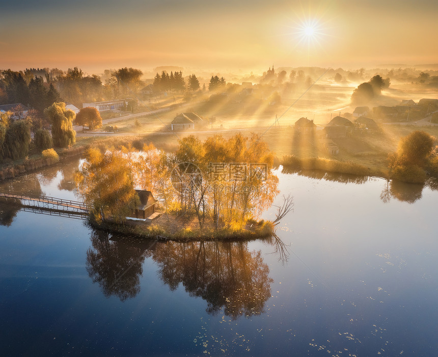 湖边小岛上有丰富多彩的树木空中景象秋天是福吉的日出美丽景色与雾中村庄金色的太阳光束水中的反射在乌克兰倒塌图片