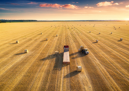农业机械日落收割粮食作物之后的查封田地和干草堆顶层视图拖拉机在卡车上装载大量干草拖车背景图片