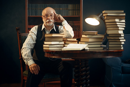 老人作家坐在桌子上里办公室有一堆书戴眼镜的老人在房间里写文学小说有烟雾和灵感老人作家坐在桌子上有书背景图片
