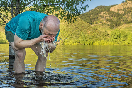 高级运动员在山湖里喷水冲洗脸部夏天早上在科罗拉多的修牙储藏室图片