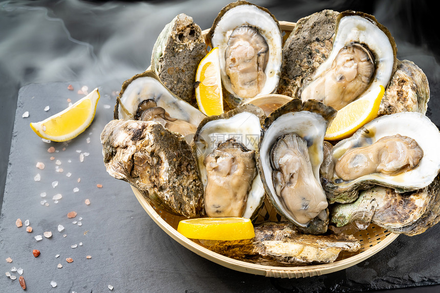 新鲜的牡蛎在黑石板上的篮子里塞柠檬新鲜的海食品和欧洲烹饪美食的概念图片