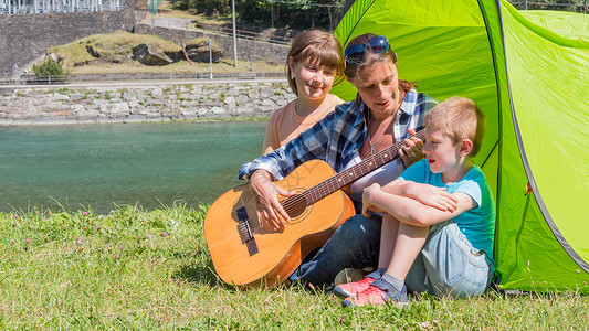 一个幸福的家庭在河边露营弹吉他在帐篷里一起唱首歌图片