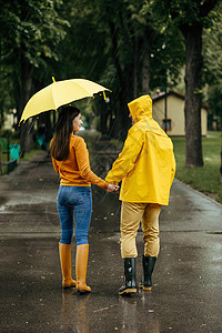 雨天在夏季公园散步的情侣和有雨伞男人和女穿着橡胶靴在路上行走巷子里的湿天气带雨伞的情夫妇在季行走背景图片