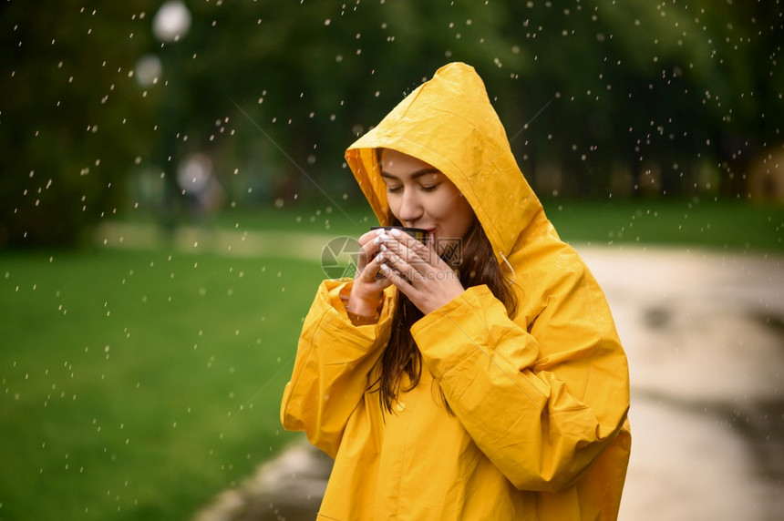 穿着雨衣的女子在天夏季公园喝热茶独自一人在走道上披着雨斗篷的女子在巷里的湿天气中穿雨衣的女子在公园喝热茶雨天穿衣的女子喝热茶图片