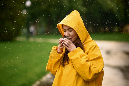 穿着雨衣的女孩穿着雨衣的女子在天夏季公园喝热茶独自一人在走道上披着雨斗篷的女子在巷里的湿天气中穿雨衣的女子在公园喝热茶雨天穿衣的女子喝热茶背景