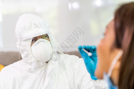 个人防护设备服检验科罗纳coronaviruscovid19的医疗人员在家里通过喉咙网向亚裔妇女进行检测在家中和医疗分娩方面提供背景图片