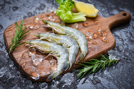 木制切板上的新虾配有迷迭香料和用于烹饪海产食品在餐厅冷冻的冰面上生虾图片