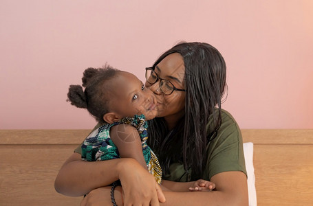 带着女儿在家工作的母亲以粉红背景为家庭关系概念工作图片