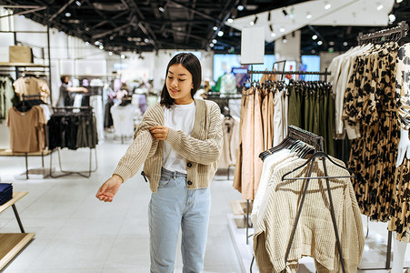 女青年在服装店试穿羊毛衫女青年在时装店商购物观光买衣服女青年在装店试穿背景图片