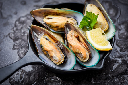 黑碗上的新鲜贝壳和加柠檬生菜的冰海产贝壳鱼蒸图片