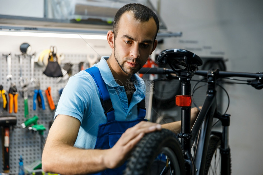 车间的自行修理工人检查轮胎穿制服的机械修车专业的自行修理服务工人检查轮胎图片
