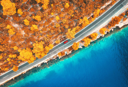 汽车天线秋天日落时美丽的橙色森林和蓝海的公路空中景象道汽车模糊水清树木秋天海岸公路的顶端旅行美丽的橙色森林和蓝海的道路空中景象背景