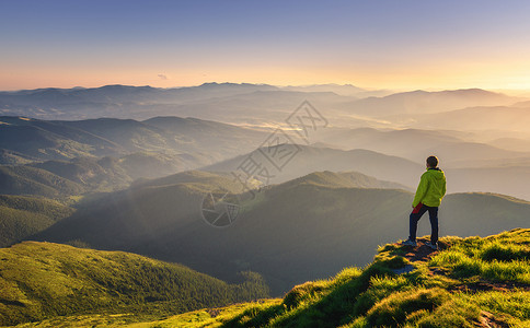草塔夫茨山峰上的运动男子在山峰上仰望着谷在欧洲秋天的多彩日落时带着阳光照耀太山峰游人迷雾的山坡森林倒塌惊人的天空和阳光倒塌的风景山峰上运背景