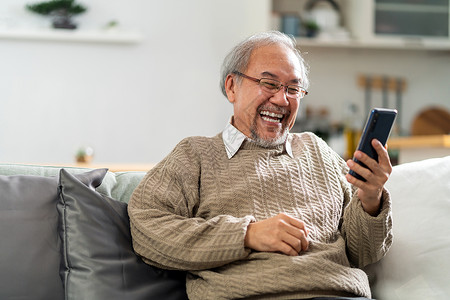坐在客厅沙发上的退休老人快乐地使用手机带着笑和容给家人打视频电话图片