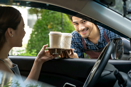 服务车司机通过窗向道服务站的顾客提供带有一次托盘和面包袋的热咖啡杯图片