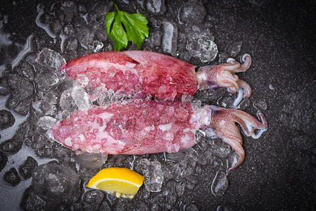 鱿鱼板冰上的生鱿鱼和黑盘海鲜市场柠檬新鱿鱼章或熟食沙拉餐厅的鱼背景