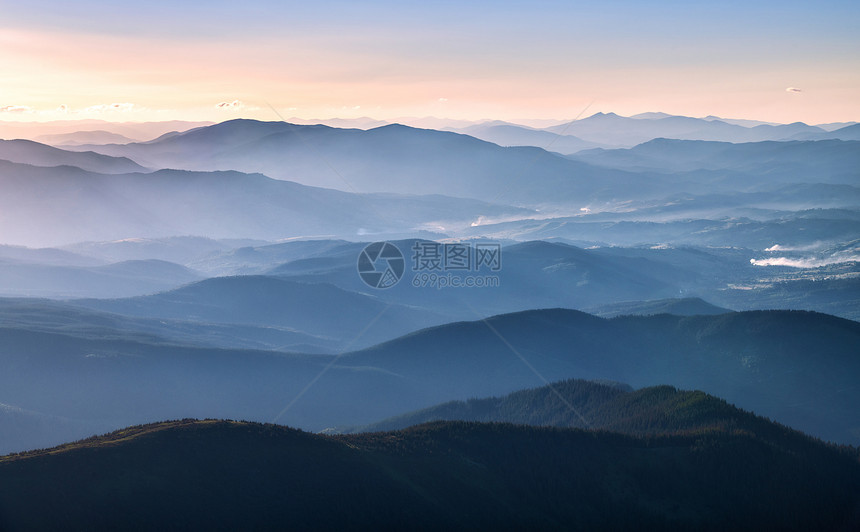 秋天日落时以明亮的太阳光照山岳风景与雾岩石森林多彩天空中的山脊以及秋天橙色阳光图片