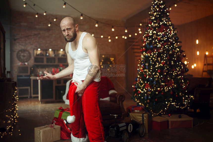 坏的圣诞老人在两腿之间戴着红色帽子下流的派对幽默不健康的生活方式穿着节日服装的胡须男子新年和酗酒坏的圣诞老人在两腿之间戴着红色帽图片