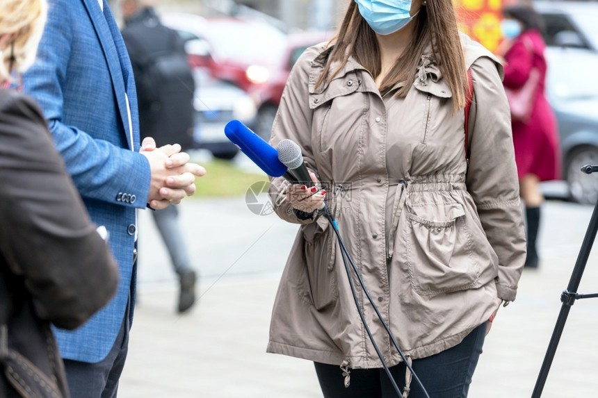 女记者戴防护面罩保防止冠状新冠19疾病在媒体采访活动中保持麦克风图片