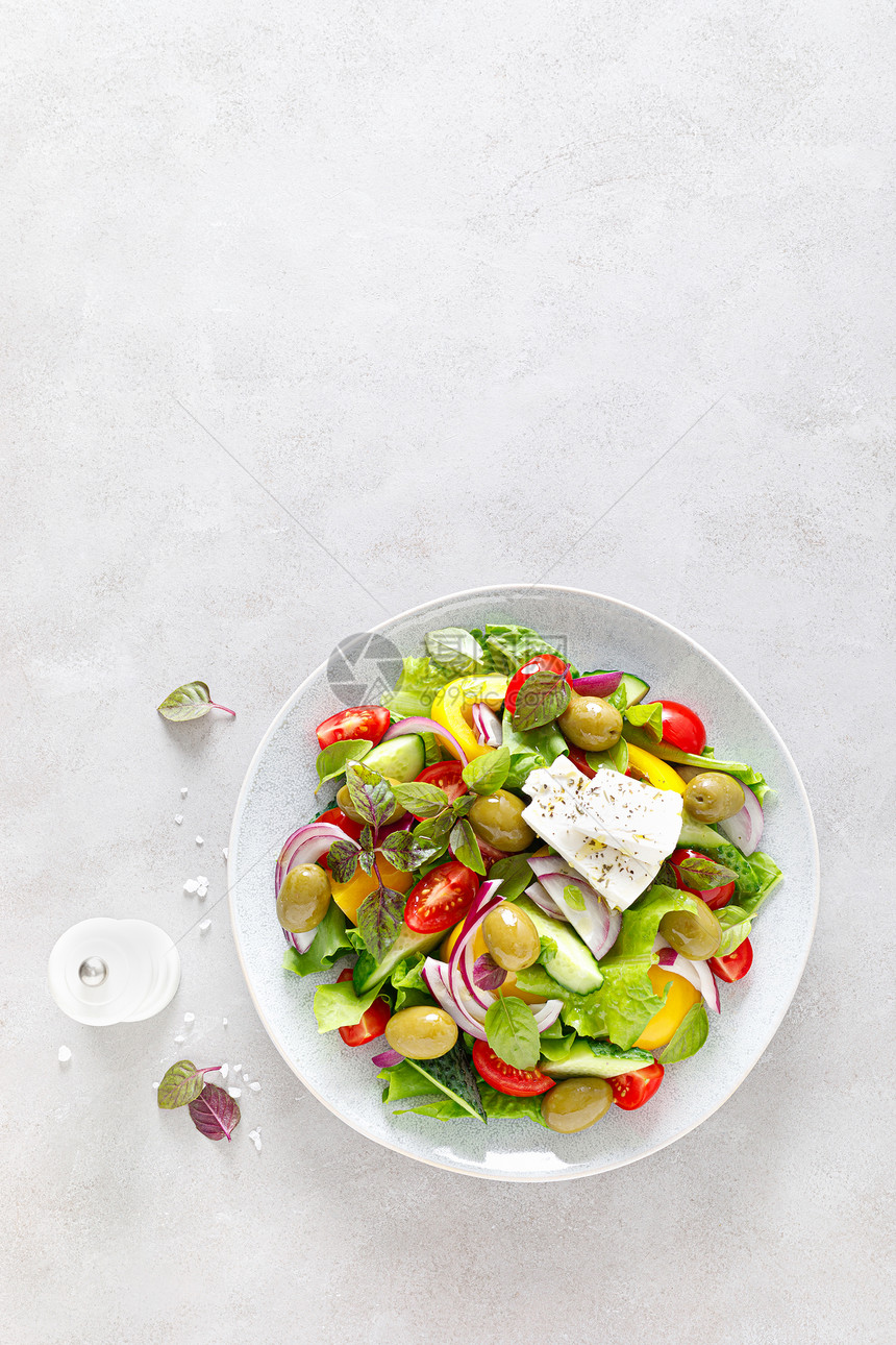 希腊沙拉新鲜蔬菜包括黄瓜西红柿橄榄洋葱铃椒奶酪生菜和草药并配有盐胡椒和橄榄油图片