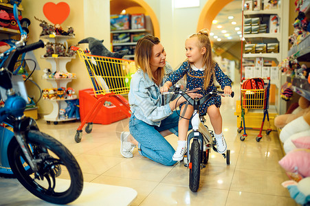 母亲和可爱的女儿在玩具店展览快乐童年家庭在商店购买自行车妈和小女孩在子的商店购买自行车妈和小女孩在子的商店购买自行车背景图片