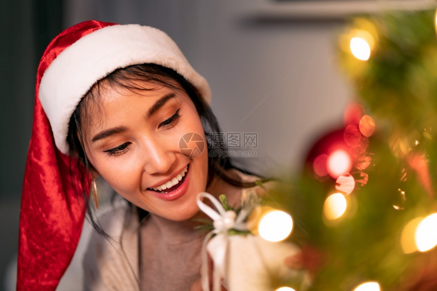 美丽的亚洲女人拿着圣诞装饰品在树上装饰图片