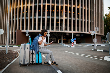 女孩坐在停车场入口处的手提箱上女旅行者在停车场附近携带行李女旅者带李女旅者在市街上携带行李女旅者坐在李箱上汽车泊入口图片