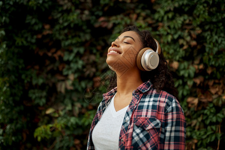 在夏季公园听音乐的女迷在户外行走女孩听耳机背景绿树图片