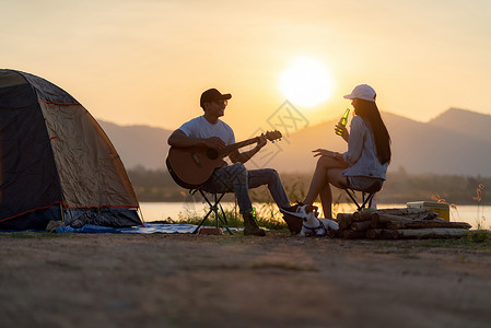 亚洲年轻成人夫妇在日落时帐篷露营地边弹吉他和喝啤酒图片