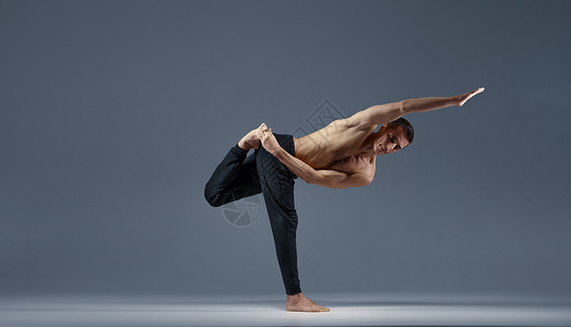 做个俗人雄瑜伽使巴兰克在一只腿上处于个难看的姿势灰色背景强壮的人在做瑜伽运动麻训练高度集中健康的生活方式瑜伽使巴兰克在一条腿上处于个难看背景