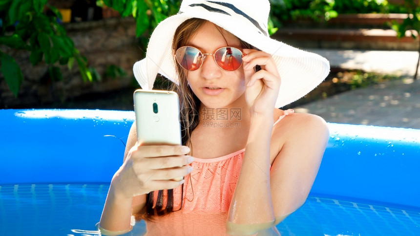 坐在游泳池和浏览互联网或社交媒体智能手机的美少女快乐暑假和期的概念美丽少女躺在游泳池和浏览互联网或社交媒体的智能手机图片