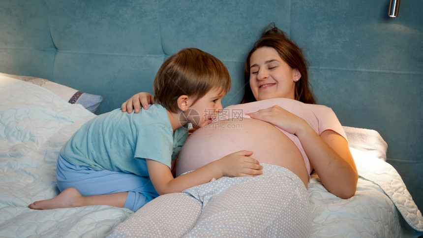 有大肚子的年轻怀孕母亲晚上和大儿子躺在床上家庭有愉快的时光在一起有期待的婴儿有大肚子的年轻怀孕母亲有期待的婴儿图片