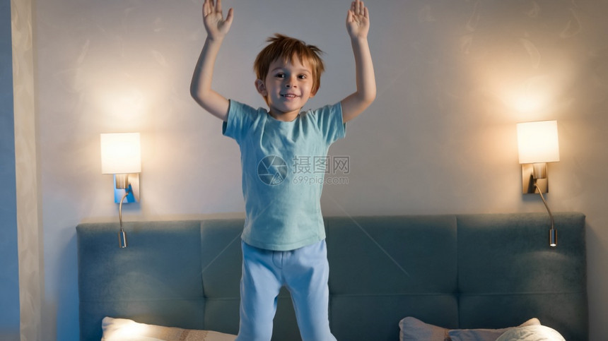 穿着睡衣的有趣小男孩晚上在父母和床上跳起和舞睡觉前没有眠和活跃的幼儿男孩穿着睡衣在父母和晚上在床跳起和舞的有趣小男孩图片