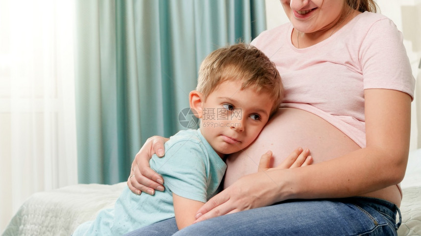 在怀孕母亲肚子里拥抱和倾听未来的婴儿在怀孕母亲肚子里拥抱和倾听未来婴儿的幼男孩肖像在怀孕母亲肚子里拥抱和倾听未来的婴儿肖像图片