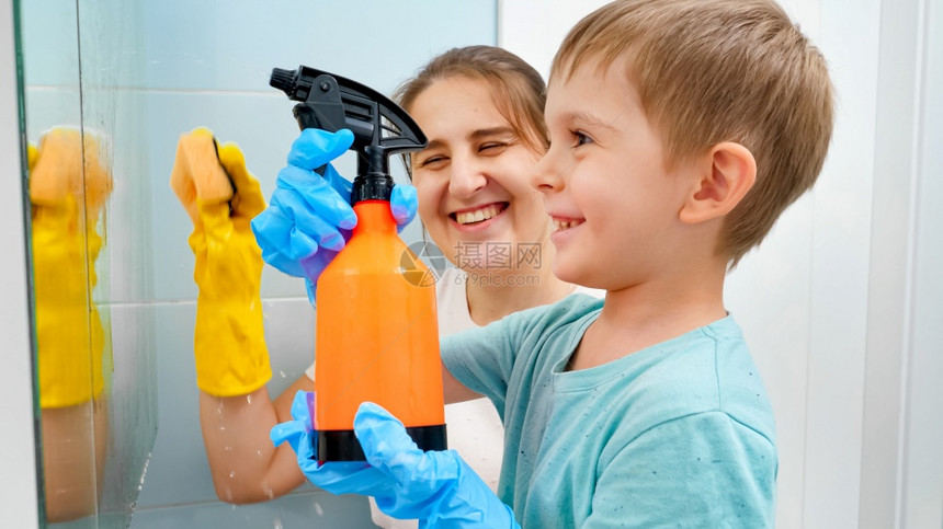 儿童小男孩在与母亲一起清洗浴室镜子时用喷洒的化学洗涤剂喷洒儿童小男孩在家中做务和清洁儿童小男孩在与母亲一起洗浴室镜子时用喷洒的化图片