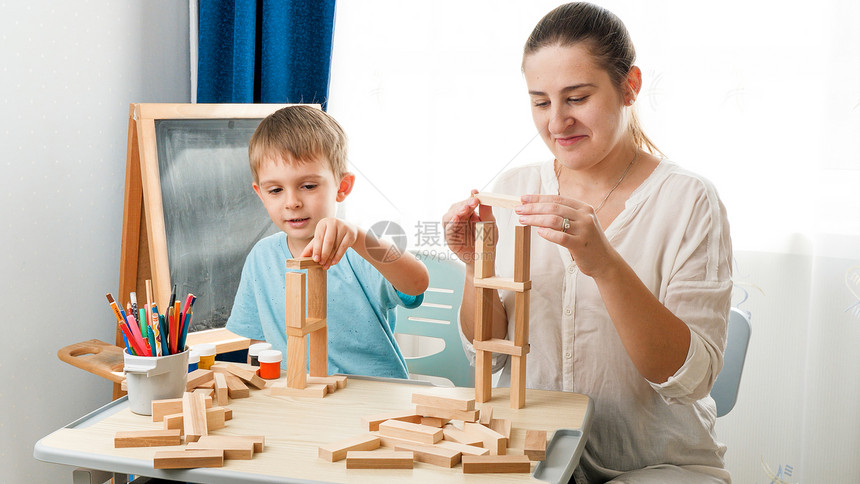 年轻母亲与小儿子玩耍在客厅用木块和砖头在桌边玩耍用木块和砖头在桌子上玩耍聪明孩子的概念和在被禁闭自我孤立期间的家庭教育养和教学年图片