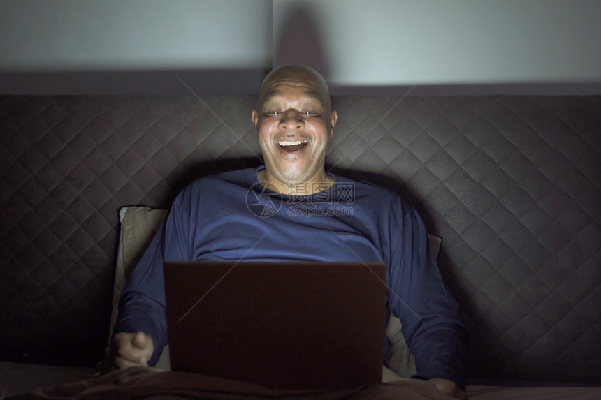 快乐的黑人老非裔美国在网上看一部有趣的电影深夜在家卧室里笑活动生方式放松时间笔记本电脑图片
