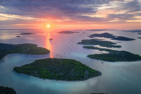 克罗地亚夏季日落时得里海美丽的小岛空中景象蓝水山上的绿树多彩天空云和橙色的太阳背景图片