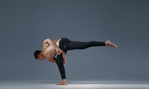 做个俗人雄瑜伽使巴兰克在一只腿上处于个难看的姿势灰色背景强壮的人在做瑜伽运动麻训练高度集中健康的生活方式瑜伽使巴兰克在一条腿上处于个难看背景