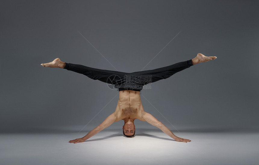 雄瑜伽站在头和手冥想灰色背景强壮的人在做瑜伽练习麻培训高度集中雄瑜伽站在头和手上图片