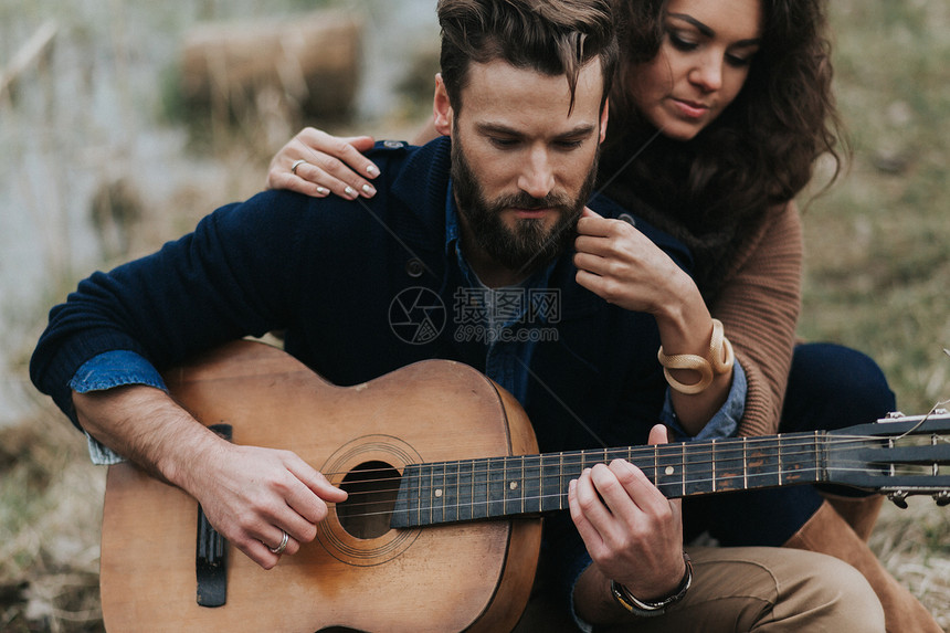 Caucasian男子在湖边与女人一起弹吉他年轻夫妇在秋天户外拥抱一个有胡子的男人和卷毛女在恋爱中ValentineDay爱和家图片