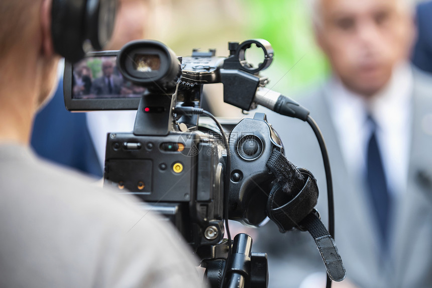 在户外记者招待会上工作的摄影机操员记者在媒体活动上采访身着正式服装的政治家或商人图片