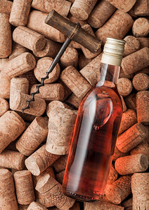 一瓶粉红玫瑰葡萄酒和古老的软木瓶子在各种葡萄酒软木背景之上图片