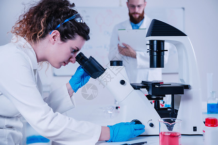 年轻女科学家在实验室做测试男科学家站在后面背景图片