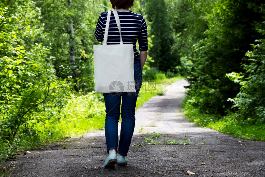 身穿条纹衣服的妇女携带空可再用购物袋模型手持帆布的妇女则用生态友好型袋模拟图片