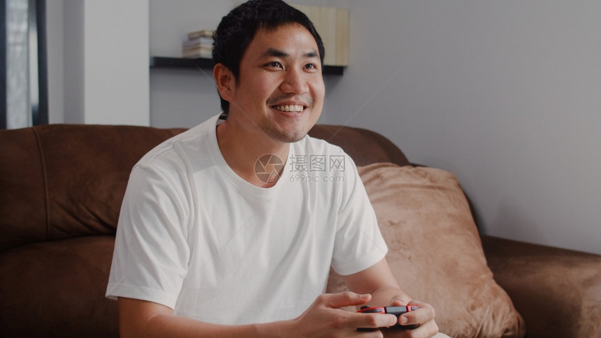 年轻的亚洲男子在客厅的电视上玩游戏男在家中沙发上休息时感到快乐男人在家里玩游戏时放松图片