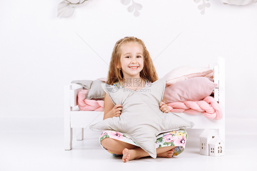 床位睡上的小女孩带着粉色麻布和枕头的在白色卧室里有一颗星在她的手上墙有工制花妇女和一天床位睡上的小女孩边有粉色麻布和枕头手制花放图片